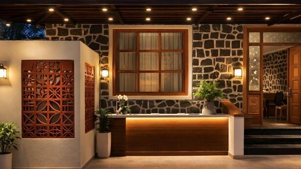 Zona de recepción con fachada de piedra, mostrador de madera y un amplio ventanal con cortinas.