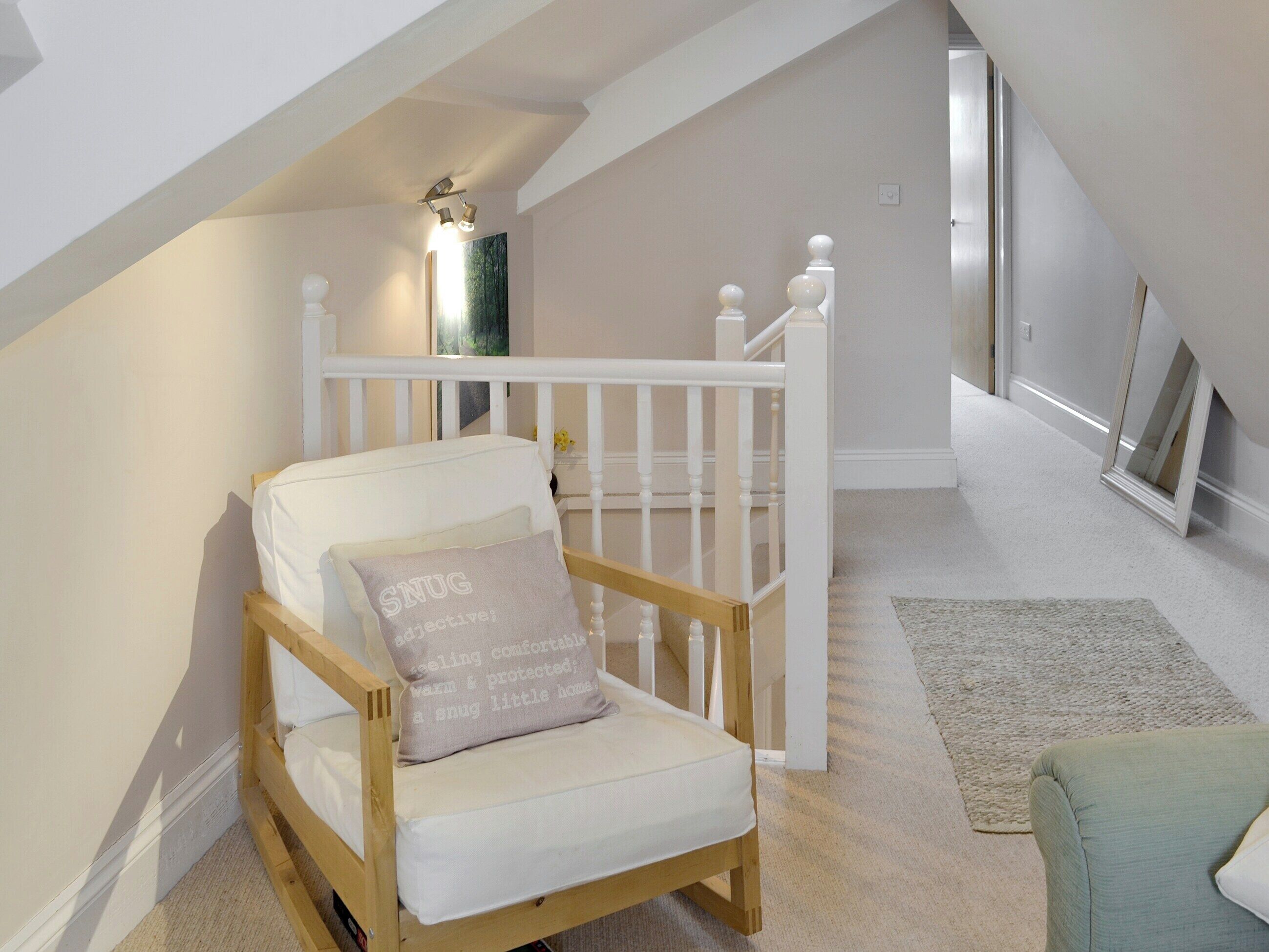 A cozy attic bedroom with a wooden bunk bed, a white crib, and a small seating area with a green cushion.