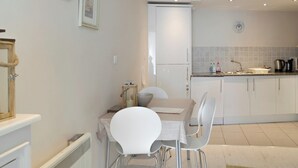 Een moderne keuken met witte kasten, een granieten aanrechtblad en een inbouwoven. Er is een eethoek met een witte tafel en stoelen.