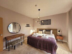 A hotel room with a large bed, bedside tables, a round mirror, a bench, and a decorative wall piece. - Marsh Marigold Cottage - UKC4642 (Dunholme, near Lincoln)