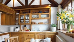 Uma cozinha com armários de madeira, uma mesa de jantar posta com xícaras, uma cafeteira e um caderno.