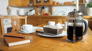 Uma mesa de madeira com uma prensa de café, uma vela, um caderno e uma chaleira.