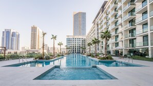 Een modern hotel met een centraal gelegen zwembad, omringd door palmbomen en hoge gebouwen.