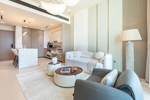 Ein modernes Wohnzimmer mit einer Couch, einem Couchtisch und einer Lampe. Im Hintergrund ist eine Küche zu sehen.
