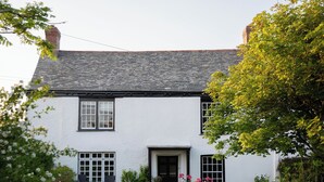 Ein weißes, zweistöckiges Haus mit schwarzem Dach, einer Haustür und Fenstern.
