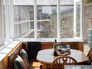 Un coin salon confortable avec une table, une bouteille de vin et des verres, donnant sur un bâtiment en pierre et un jardin.