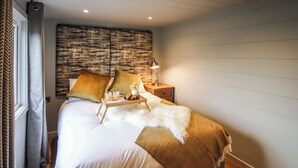 A neatly made bed with a white and brown blanket, a bedside table with a lamp, and a wall with a textured pattern. - 2 bedroom accommodation in Rhayader and the Elan Valley (Rhayader and the Elan Valley)