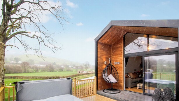 A wooden deck with a hot tub, a hanging chair, and a view of the countryside. - 2 bedroom accommodation in Rhayader and the Elan Valley (Rhayader and the Elan Valley)