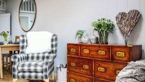 A room with a plaid armchair, a wooden dresser with brass handles, a mirror, and a vase with flowers. - 2 bedroom accommodation in Rhayader and the Elan Valley (Rhayader and the Elan Valley)