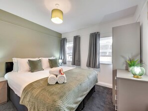 Een hotelkamer met een bed, nachtkastje, bureau, lamp en een raam met gordijnen.