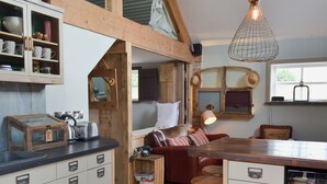 Une cuisine rustique avec des meubles en bois, une fenêtre à cadre en bois, un luminaire suspendu et une petite table avec une bouilloire.