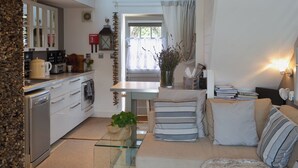 Un espacio habitable compacto con kitchenette, comedor y zona de estar con sofá y cojines.
