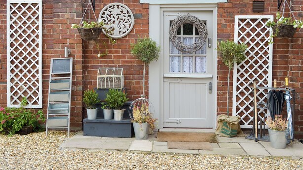 Una casa de ladrillo con una puerta blanca, una corona decorativa y plantas en macetas.