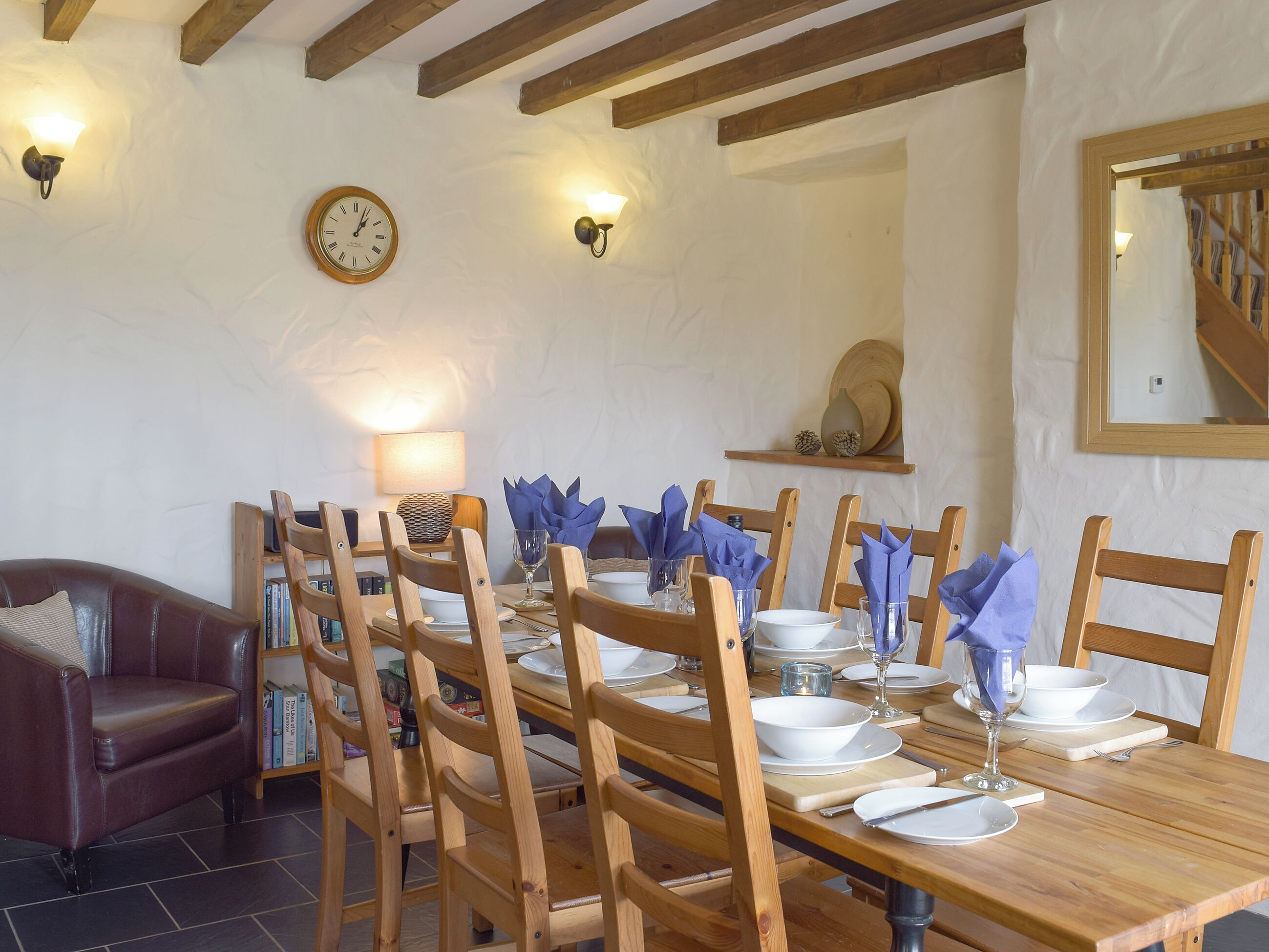Un comedor con sillas de madera, una mesa de madera dispuesta para una comida, un reloj y luces fijadas a la pared.