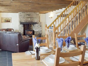 Ein gemütliches Wohnzimmer mit Kamin aus Stein, einer Ledersofa, einem Holzesstisch für vier Personen und einer Holztreppe.