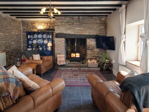 A cozy living room with leather sofas, a stone fireplace, and a television mounted on the wall. - 2 bedroom accommodation in Kidwelly (Kidwelly)