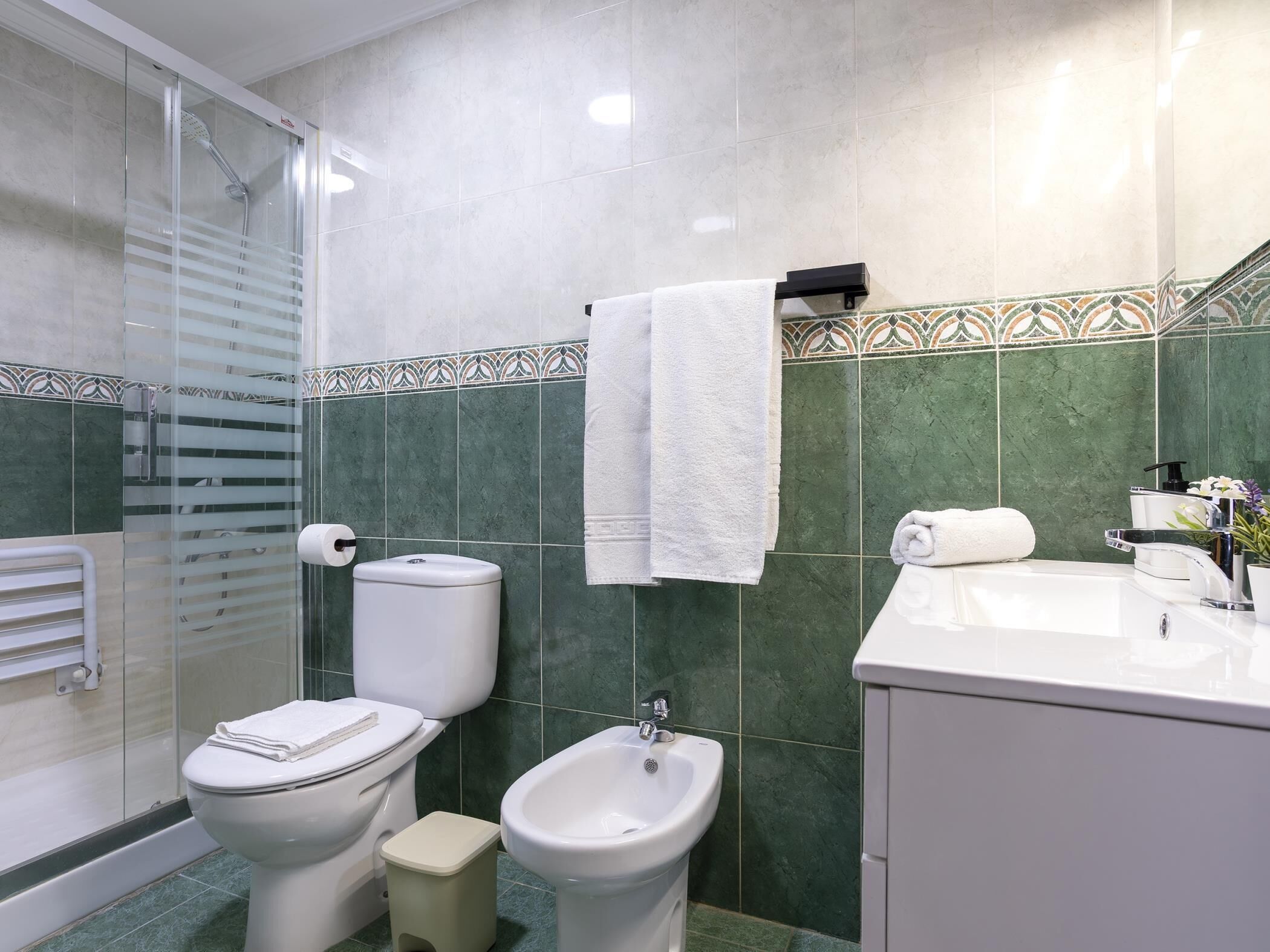 Ein Badezimmer mit Toilette, Bidet und Waschbecken, mit grünen Fliesen und weißen Armaturen.