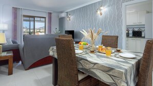 A dining area with a table set for two, a sofa, and a view of the cityscape through a window. - Sunstay Adriana Flat II Fuengirola (Fuengirola)