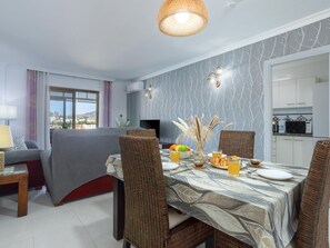 A dining area with a table set for two, a sofa, and a view of the cityscape through a window. - Sunstay Adriana Flat II Fuengirola (Fuengirola)