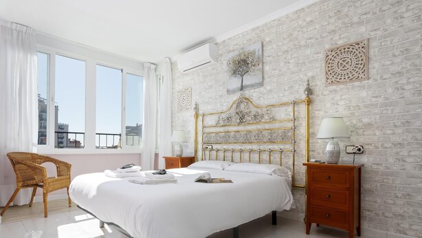 A bedroom with a bed, a chair, a nightstand, a lamp, and a wall with a decorative piece. - Sunstay Adriana Flat II Fuengirola (Fuengirola)