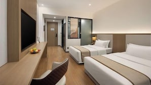 A hotel room with a bed, a desk with a flat-screen TV, a chair, and a small table with fruit. - JingdezhenGrand Skylight Yue Hotel (Guyao Folk Custom Expo Area) (Jingdezhen)