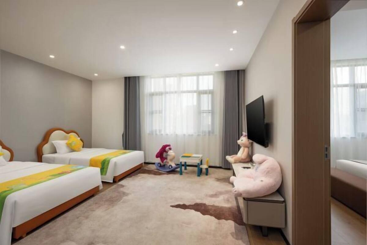 Een hotelkamer met twee bedden, een televisie, een klein tafeltje met speelgoed en een groot raam.