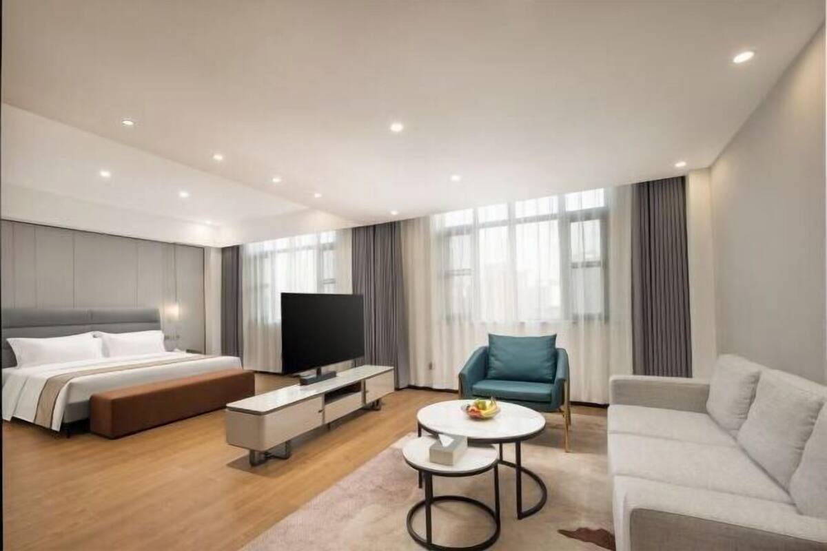 Een moderne hotelkamer met een bed, een televisie, een bank, een stoel en een klein tafeltje.