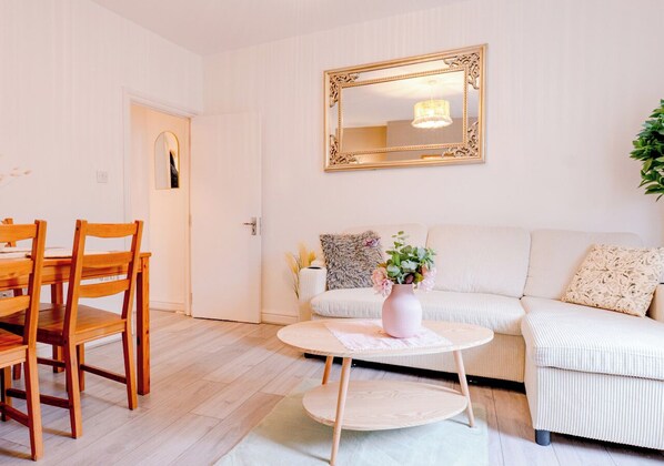 Un salon avec un canapé blanc, une table basse ronde et une table à manger en bois, accompagnée de chaises.