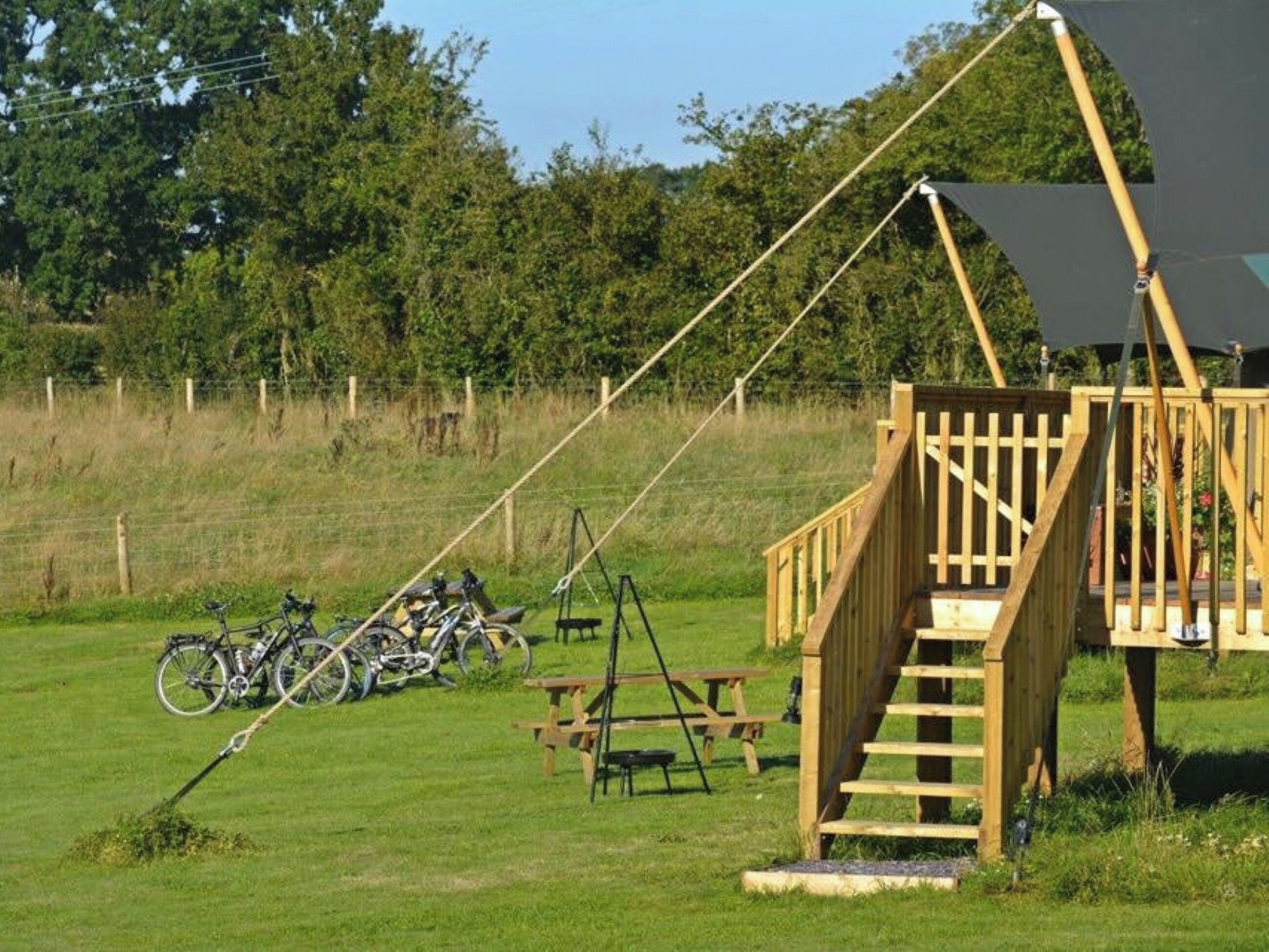 A wooden staircase leading to a platform, surrounded by a grassy field with bicycles parked nearby.