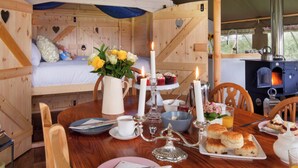 A cozy wooden cabin with a bed, a dining table set with breakfast, and a wood-burning stove. - 5 Lower Keats Glamping - UKC4742 (Tytherleigh, near Axminster)