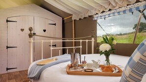 A cozy bedroom with a wooden wardrobe, a bed with a tray of breakfast, and a window with a view of the countryside. - 5 Lower Keats Glamping - UKC4742 (Tytherleigh, near Axminster)
