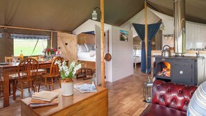 A cozy cabin interior with a dining area, a living room with a leather sofa, a wooden dining table, and a kitchen with a wood-burning stove. - 5 Lower Keats Glamping - UKC4742 (Tytherleigh, near Axminster)