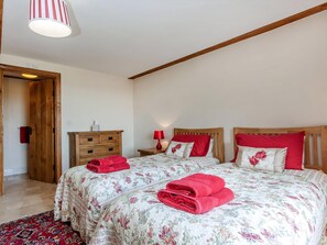 A bedroom with two beds, wooden headboards, a nightstand with a lamp, a wooden dresser, and a red rug. - Orchard Cottage - UKC4805 (Bishops Nympton)