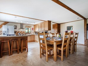 A kitchen with wooden cabinets, a dining table with chairs, and a bar area with stools. - Orchard Cottage - UKC4805 (Bishops Nympton)