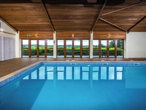 An indoor swimming pool with wooden ceiling beams, large sliding glass doors, and a view of the countryside. - Orchard Cottage - UKC4805 (Bishops Nympton)