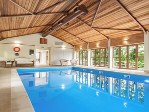 A large indoor swimming pool with wooden beams on the ceiling, a lifebuoy on the wall, and a view of greenery outside. - Orchard Cottage - UKC4805 (Bishops Nympton)