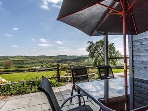An outdoor seating area with a table and chairs, an umbrella, and a view of rolling hills. - Orchard Cottage - UKC4805 (Bishops Nympton)