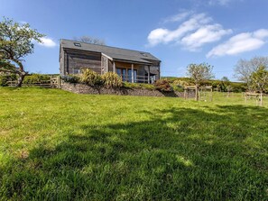 A modern two-story house with a stone foundation, a wooden deck, and a well-maintained lawn. - Orchard Cottage - UKC4805 (Bishops Nympton)