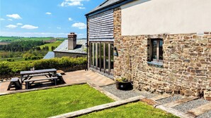 A stone building with a large patio, a picnic table, and a view of the countryside. - Barn Cottage - UKC4804 (Bishops Nympton)