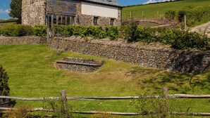 A stone house with a sloped roof, a stone wall, and a grassy yard. - Barn Cottage - UKC4804 (Bishops Nympton)