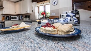 A kitchen with a granite countertop, a clock on the wall, and a window with a view of greenery. - Barn Cottage - UKC4804 (Bishops Nympton)