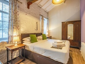 A bedroom with a large bed, wooden headboard, a nightstand with a lamp, a wardrobe, and a window with curtains. - The Old Workshop - UKC4838 (New Mills)