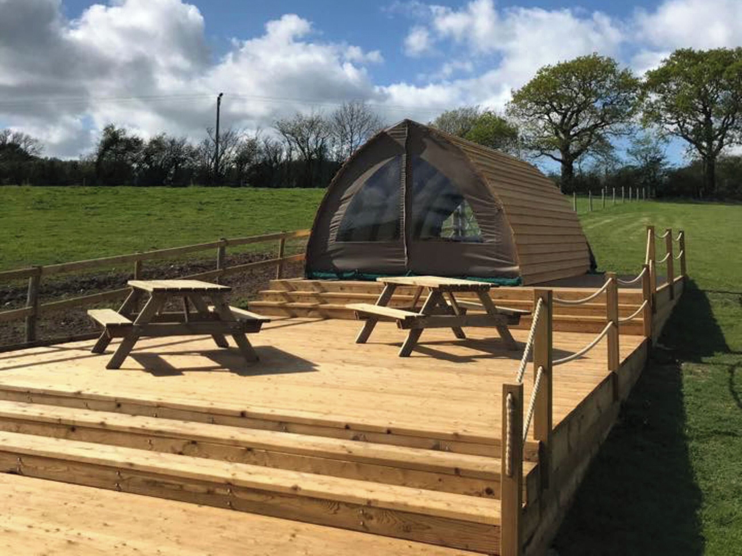 A wooden deck with picnic tables and a tent structure.