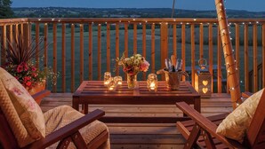 Una terraza de madera con una mesa dispuesta para dos, adornada con velas, un florero con flores y una botella de champán.