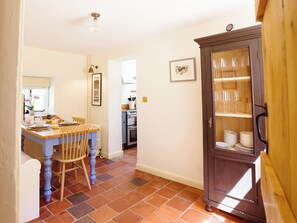 A dining area with a wooden table and chairs, a cabinet with glassware, and a kitchen in the background. - 2 bedroom accommodation in Worstead (Worstead)