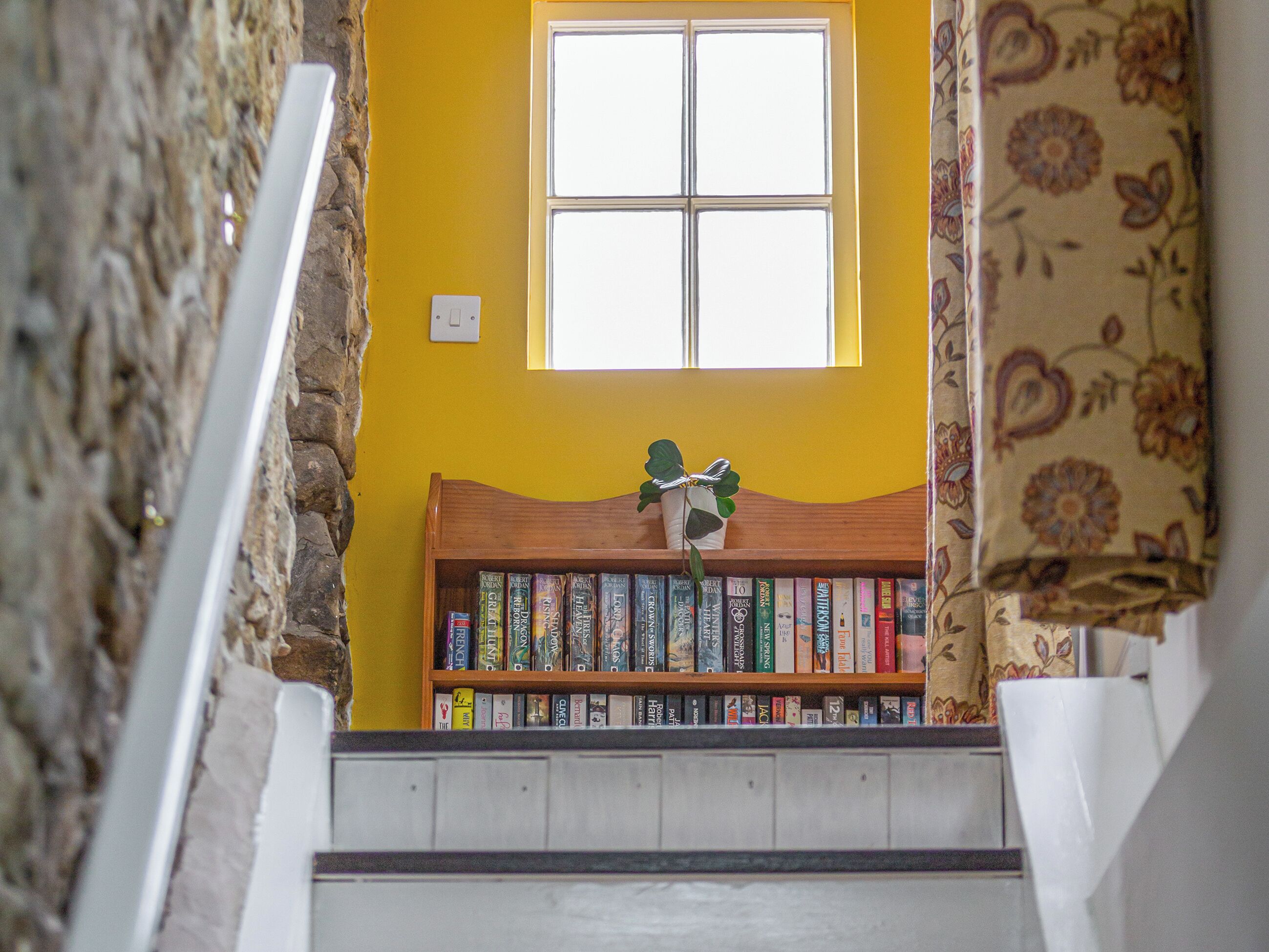 Eine Treppe mit einer Holzhülle, gefüllt mit Büchern, einem Fenster mit weißem Rahmen und einer Steinwand.