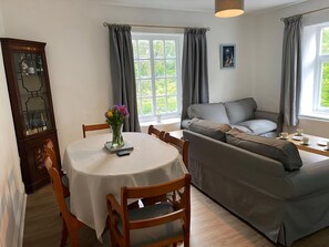 A room with a dining table, chairs, a sofa, a cabinet, and a window with curtains.