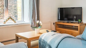 Un salon chaleureux avec un meuble TV en bois, un téléviseur à écran plat, une petite plante et un joli porte-bougie placé près de la fenêtre.