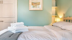 Un lit bien fait, avec du linge de lit blanc, une pile de serviettes pliées et un tableau représentant un paysage, accroché au mur.