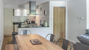 Een moderne keuken met witte kastjes, een houten eettafel en een grijze bank.